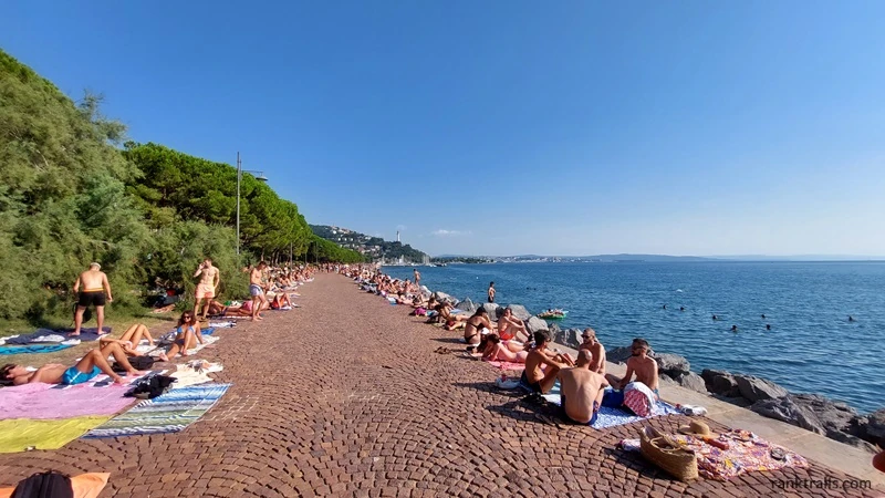 People sunbathing and swimming along the Barcola promenade in Trieste, Italy.