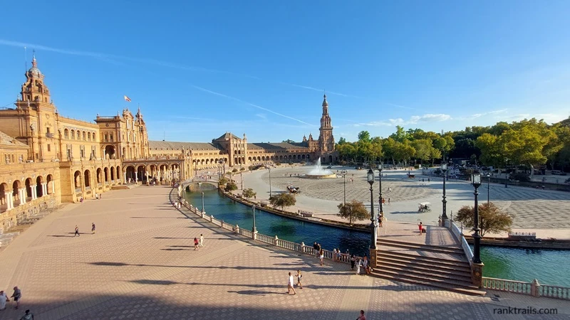 Daytime view of Plaza de España in Seville, Spain, with the central fountain and canal under a clear blue sky.