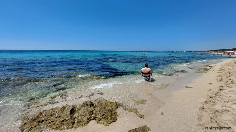 Man sitting on the edge of the sea at Porto Cesareo beach in southern Italy, used to illustrate SEO alt text for travel images.