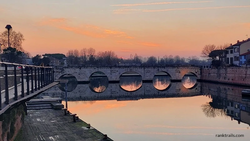 Sunset view of the Tiberio Bridge reflecting on the calm water in Rimini, Italy used as an example of alt text for travel photos.