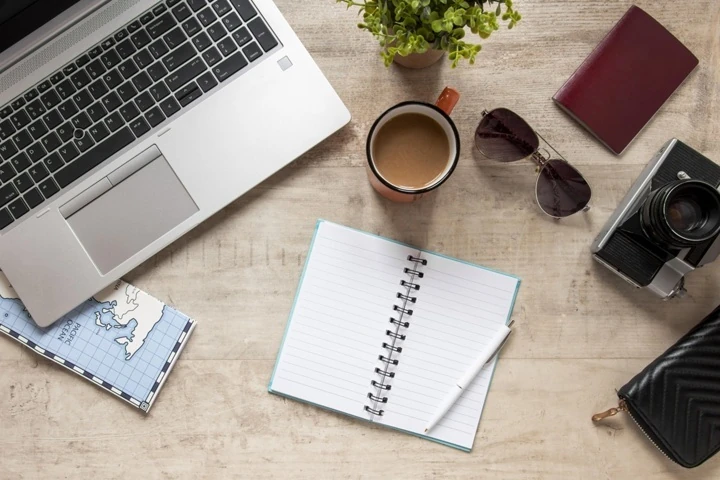 Flat lay of travel blogging essentials including a laptop, notebook, camera, and coffee, symbolizing travel SEO and content creation.