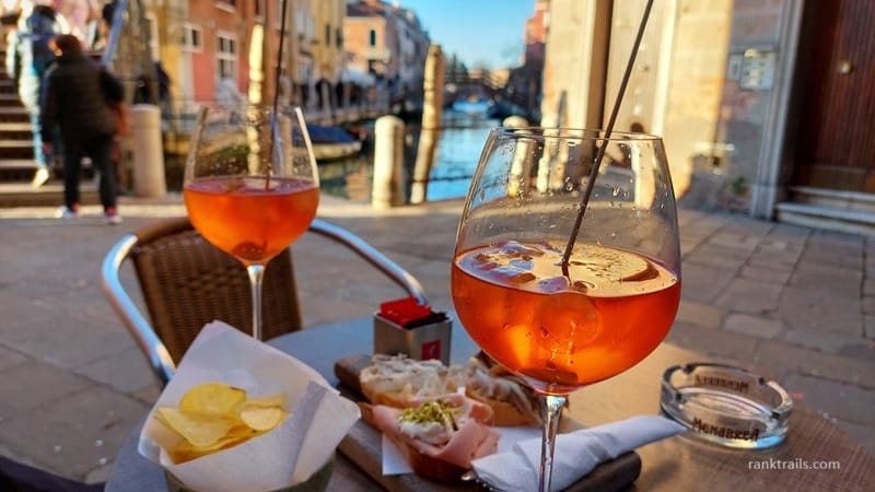 Aperol Spritz drinks and cicchetti by a canal in Venice, Italy, during a traditional evening aperitivo