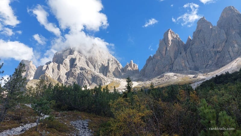 Rocky peaks of the Dolomites near Seceda in Italy under a blue sky with low clouds and alpine forest in the foreground